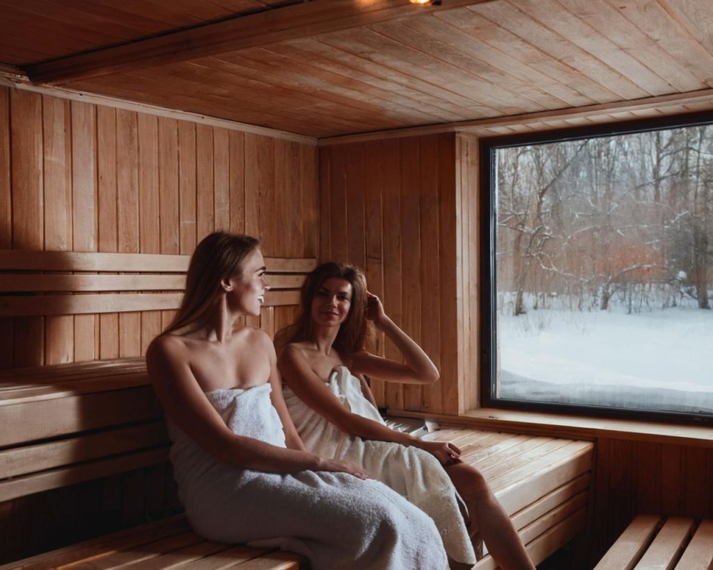 Zwei Frauen sitzen entspannt in einer Sauna und unterhalten sich.