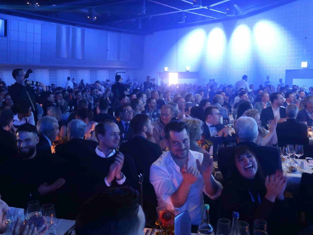 Gäste sitzen an festlich gedeckten Tischen im blau erleuchteten Saal.