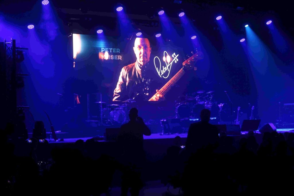 Auf der großen Leinwand erscheint die Band im Scheinwerferlicht.