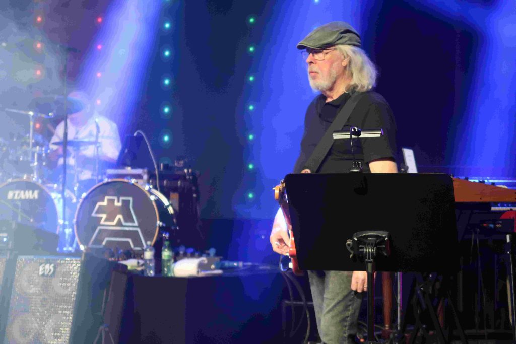 Gitarrist der Rockband mit langen Haaren und Schiebermütze auf der Bühne.