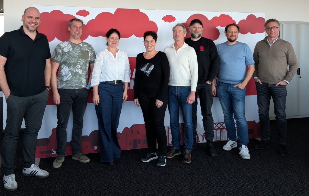 Männer und Frauen der Jury stehen vor einer Wand mit den Motiv der Bauhelden GmbH.